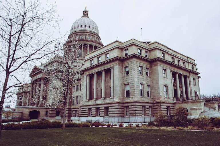 Low angle view of a historic capitol building with a dome, columns, and surrounding trees.